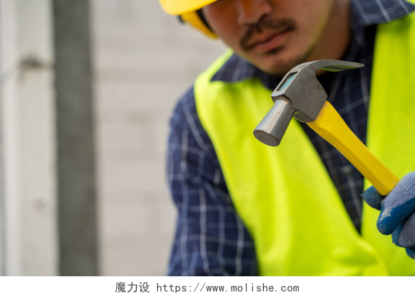 一个男工人拿着锤子在锤东西工业工人在在建房屋中建筑外墙,用铁锤在水泥中砌筑砖. 
